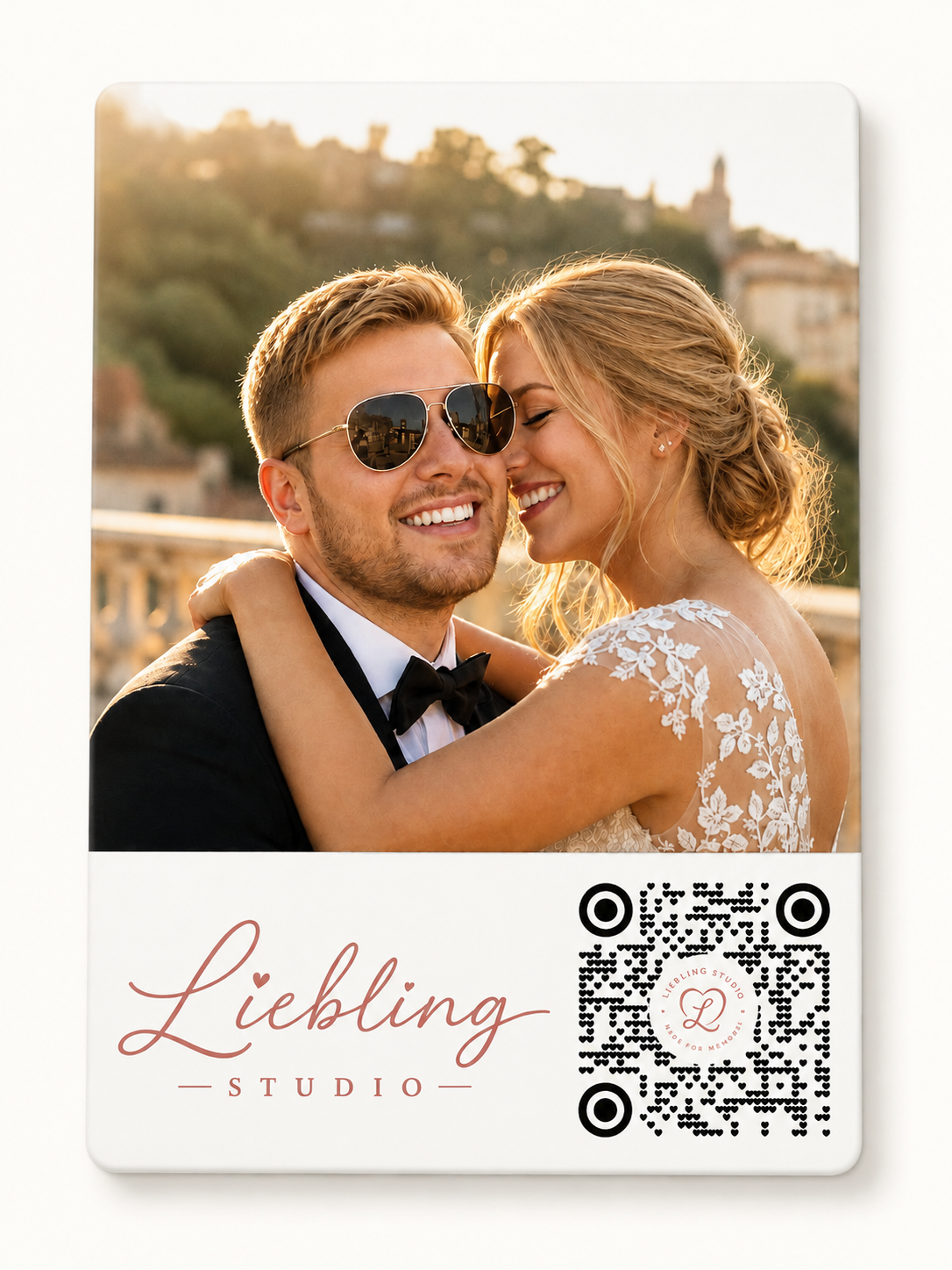 A custom wedding photo card featuring a printed photograph of a smiling couple at sunset, with the text 'Liebling STUDIO' in rose gold script and a black-and-white QR code on a white card with rounded corners.